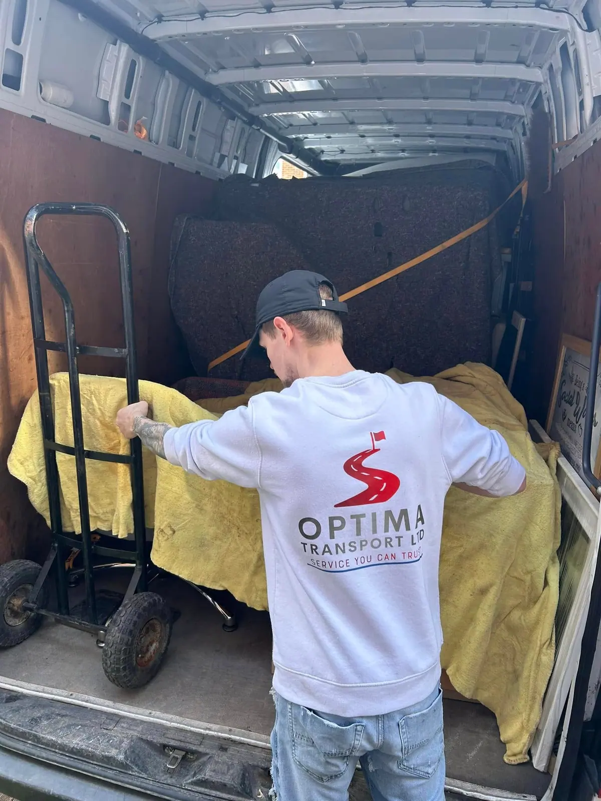 Optima Transport team member covering furniture with a blanket beside a sack truck during a Manchester flat clearance